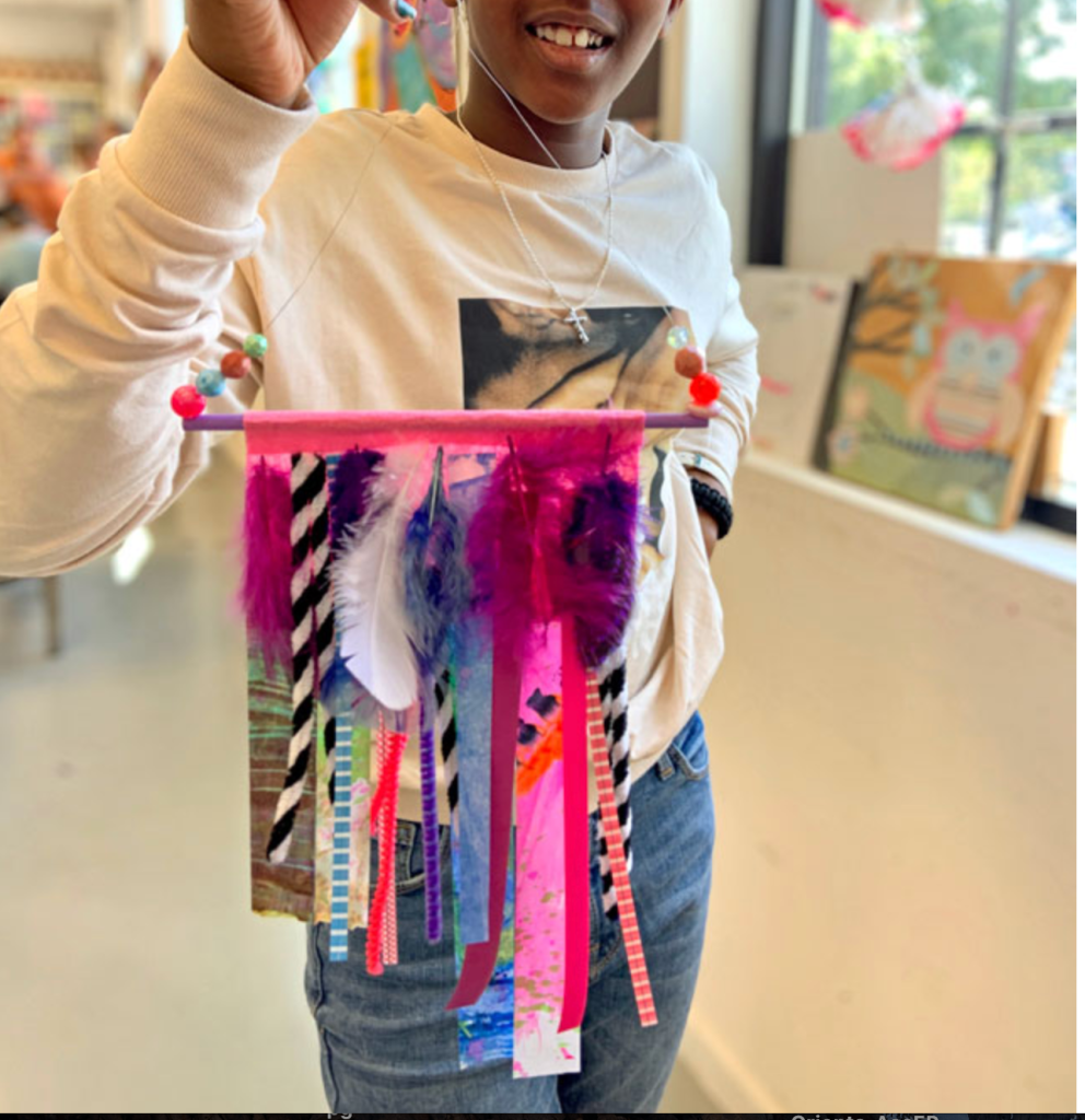 Telar con diferentes materiales unidos en un palo de madera pintado y ensamblado con un alambre lleno de cuentas de colores.